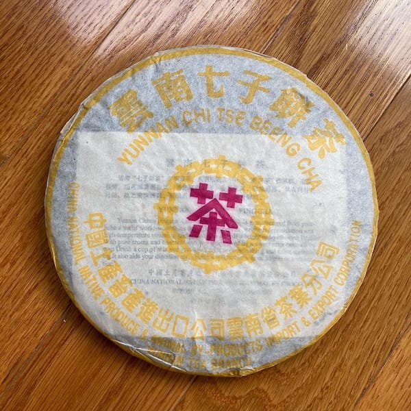 the compressed tea cake wrapped in white paper, on the wrapper is yellow Chinese characters along with a single purple character