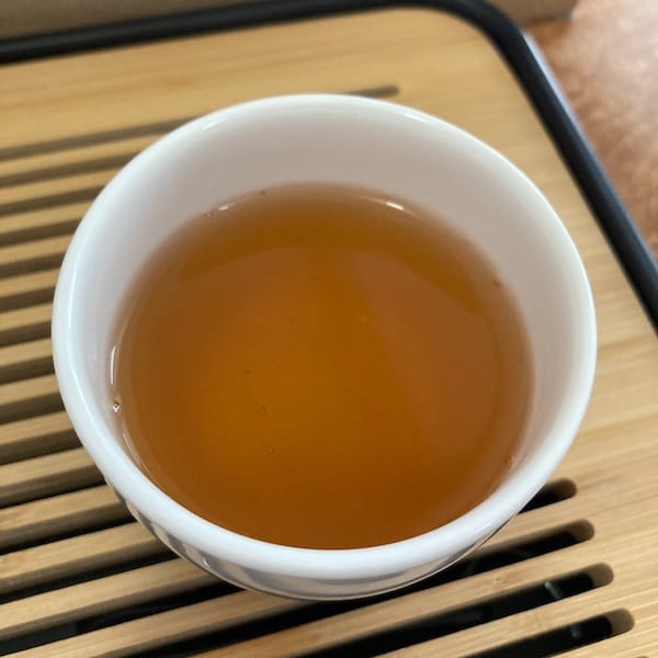 the tea, redish orange in color in a white cup on a tea tray