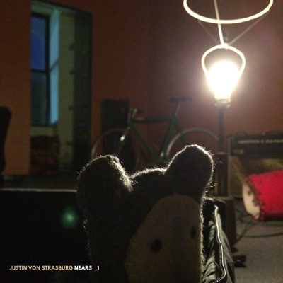 The album cover for (20180807) nears. The album cover is a close up photo which is focused on a plush toy I have, named Action, sitting in my snare drum case on the floor. The room, my old band DEBOUCH's practice space, also has a bike and a light in it that is in view.