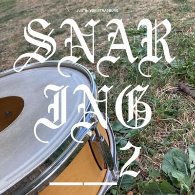 The album cover for snaring__2. It is a photo of a snare drum sitting on the grass with the album title displayed on top if large stylized text.