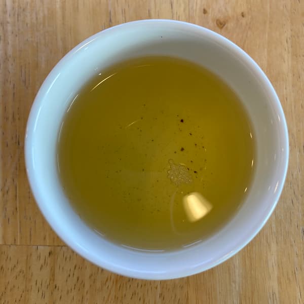 the tea, yellow in color, in a small white cup