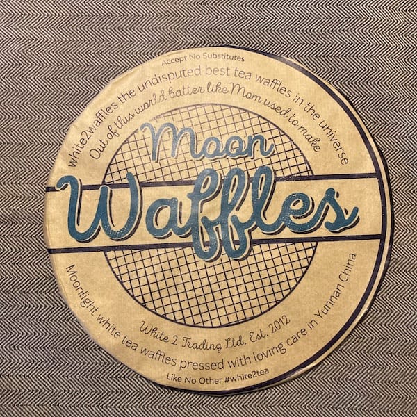 the compressed tea cake in a tan paper wrapper, on the wrapper there is a grid of lines along with the stylized words Moon Waffles