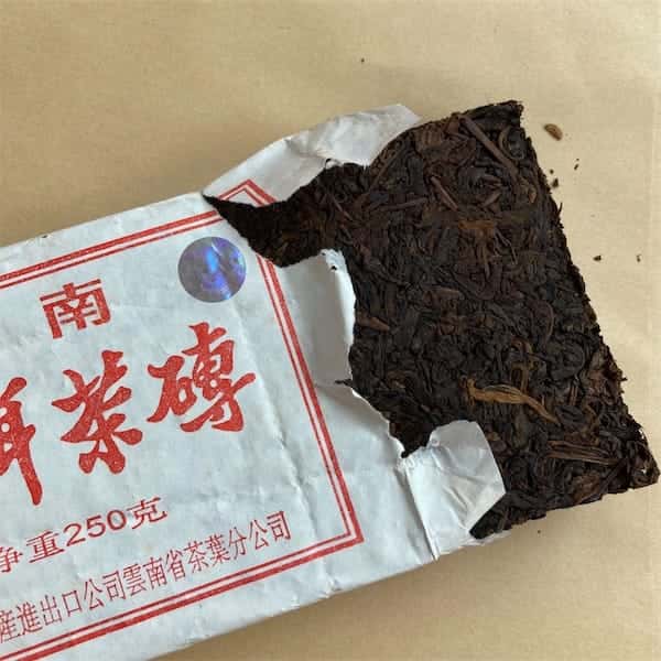 the compressed tea brick popping out of it's white paper wrapper, on the wrapper there is red border and red colored Chinese characters
