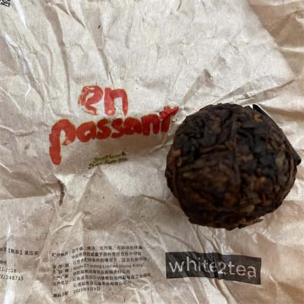 the compressed tea mini sitting on it's tan colored wrapper that has the words En Passant written in red marker