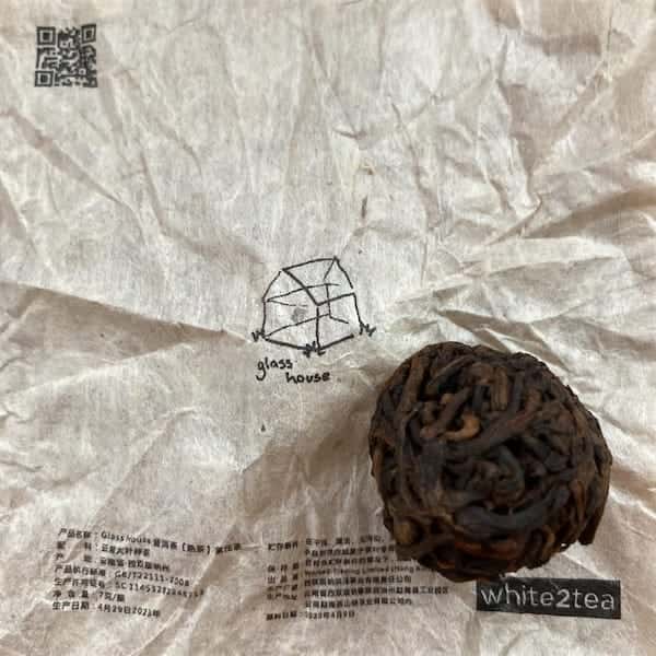 the compressed tea mini of dark brown and tan leaves sitting on it's tan wrapper with a handrawn house on it