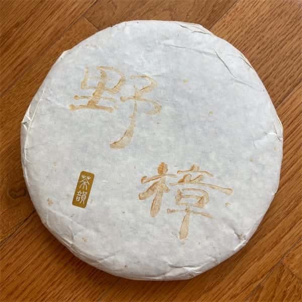 the compressed tea cake in a white paper wrapper, on the wrapper there are Chinese characters