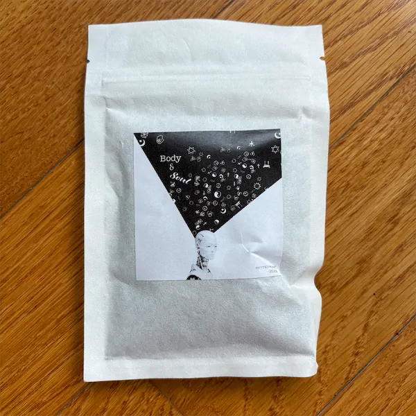 a white mylar package with a label that displays a black triangle shape, with smaller white shapes and the words Body & Soul enclosed in it, coming out of a white robot's head