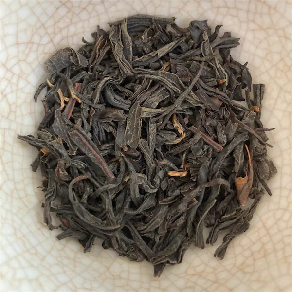 the tea, dark grayish brown and caramel colored leaves, in a white porcelain gaiwan